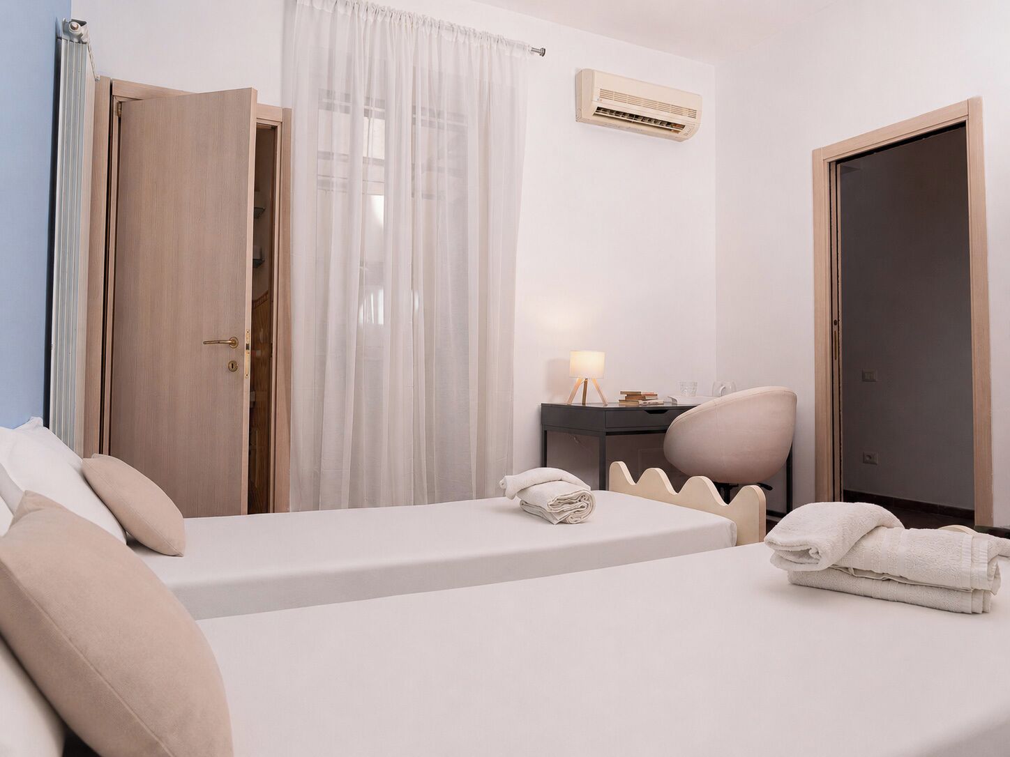A hotel room with a bed, a desk, a chair, a wardrobe, and an air conditioning unit.