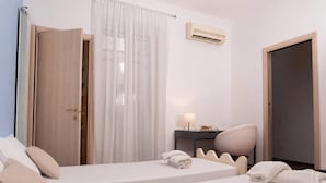 Una habitación de hotel con cama, escritorio, silla, armario y aire acondicionado.