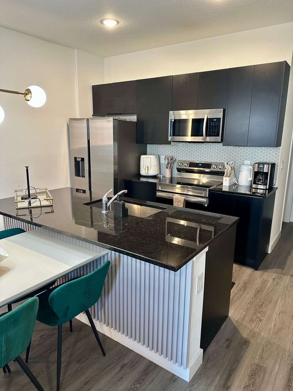 A modern kitchen with a central island, stainless steel appliances, and a dining area with a white table and teal chairs.