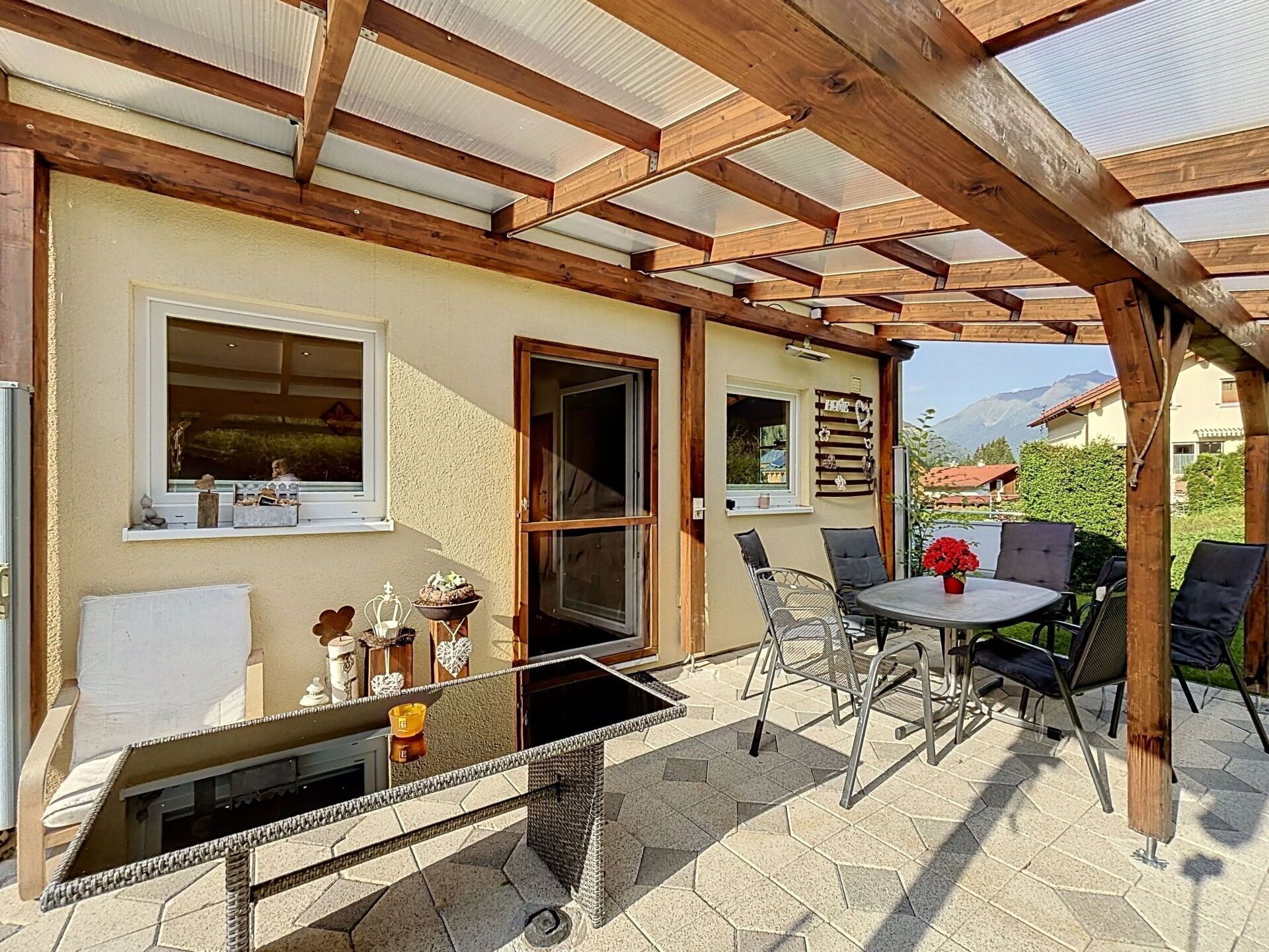 Eine Terrasse im Freien mit einer Holzpergola, einem Tisch mit Stühlen und einem Fenster mit Dekoration.