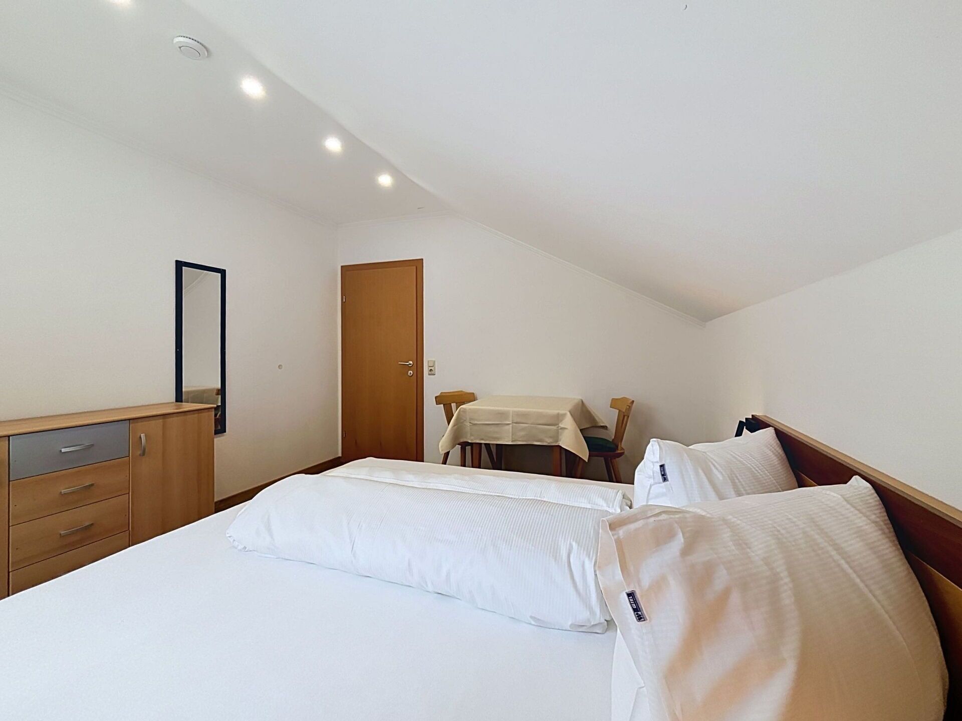 Una camera da letto con un letto, una cassettiera in legno, una scrivania con una sedia e una porta.