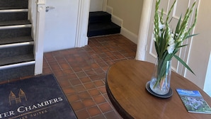 L’entrée d’un hôtel, avec un escalier, un lustre, une porte et un paillasson.