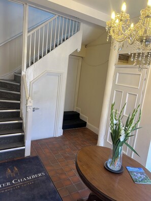 A hotel entrance with a staircase, a chandelier, a door, and a welcome mat.