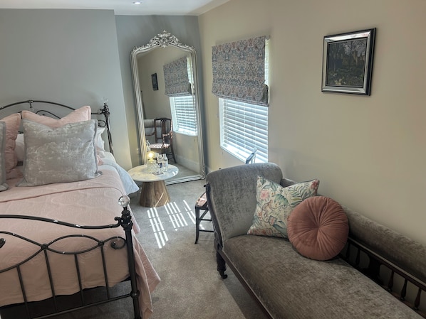 A bedroom with a bed, a sofa, a mirror, and a window with blinds.