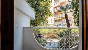 A balcony with a white metal railing, a tiled floor, and a view of a residential area with trees and parked cars. - Cosy apartment for 3 guests with WIFI, A/C, TV, balcony and pets allowed (Santo Stefano Al Mare)