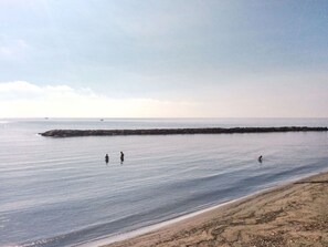 Ein Strand mit ruhigem Wasser, einem steinernen Wellenbrecher und einem Sandstrand.