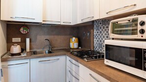 A kitchen with white cabinets, a gas stove, a microwave, and a kettle. - Cosy apartment for 3 guests with WIFI, A/C, TV, balcony and pets allowed (Santo Stefano Al Mare)