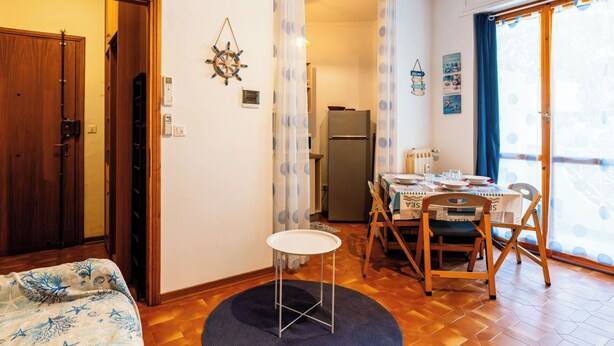 A compact room with a bed, a dining table set for two, a refrigerator, and a view through a door. - Cosy apartment for 3 guests with WIFI, A/C, TV, balcony and pets allowed (Santo Stefano Al Mare)