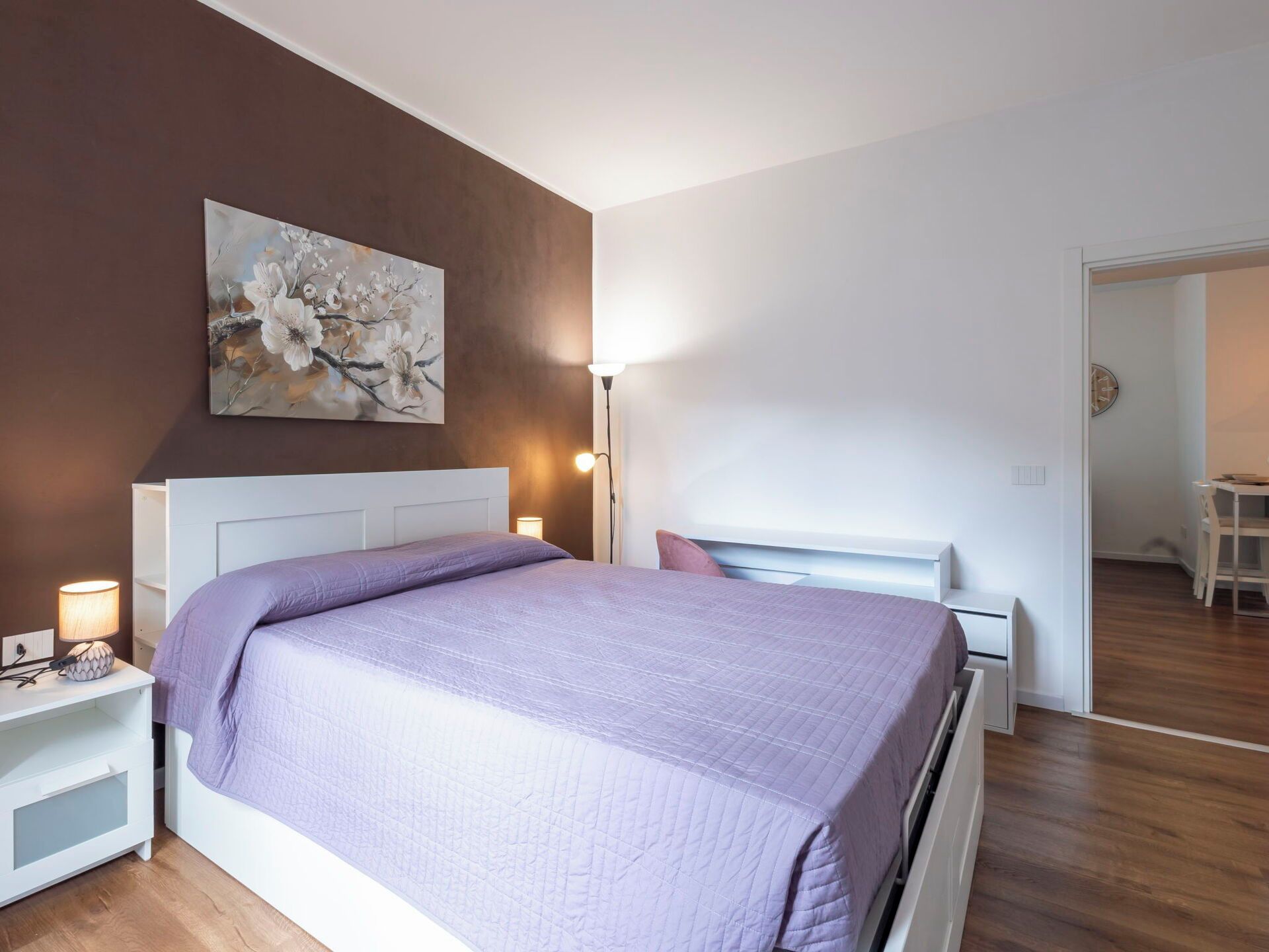 A modern bedroom with a bed, bedside tables, a lamp, and a painting on the wall.