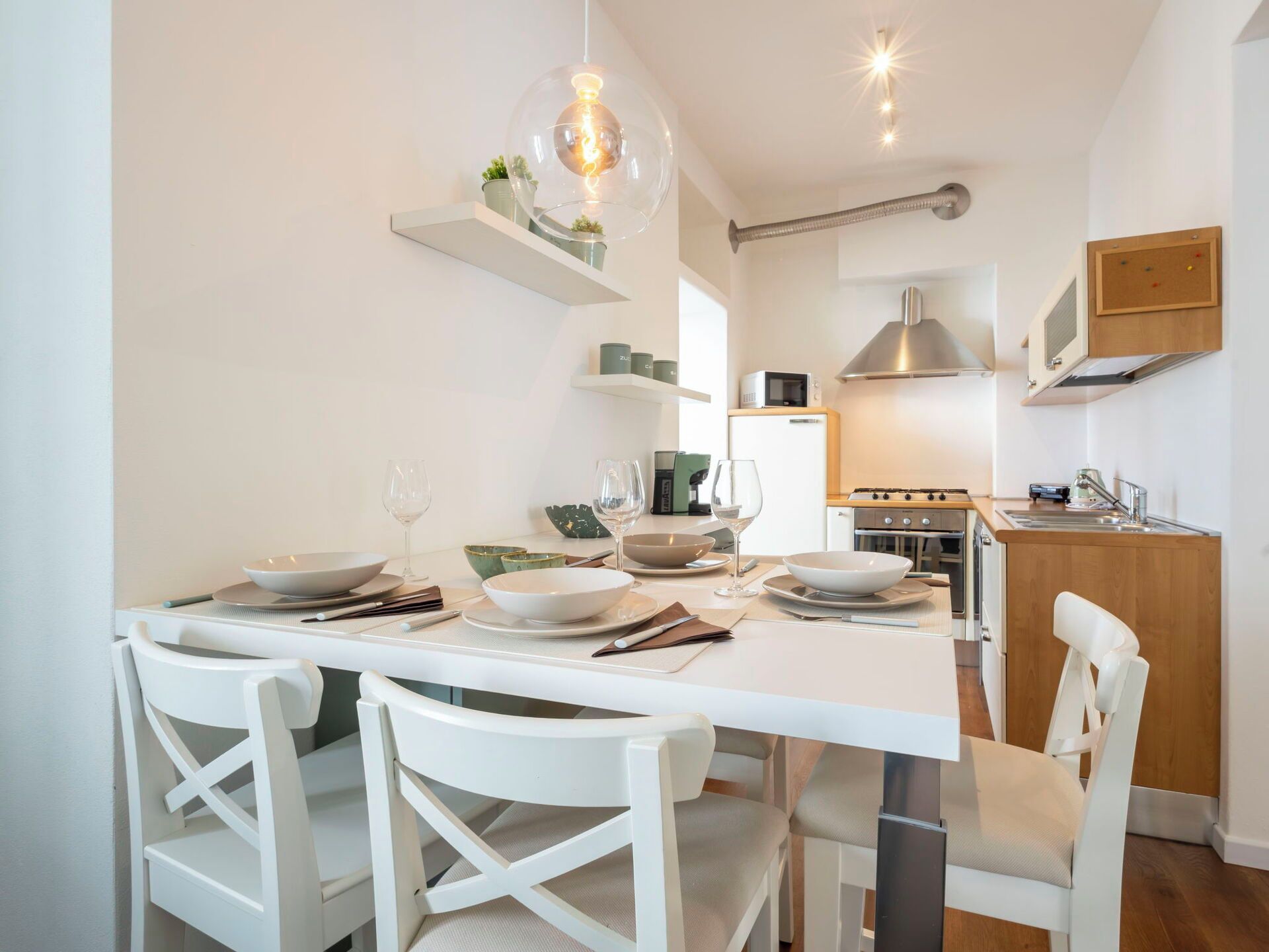 Une cuisine moderne avec des meubles blancs, une table à manger pour quatre personnes et un luminaire suspendu.