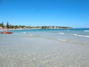 Ein Strand mit klarem Wasser, einem roten Boot und Gebäuden im Hintergrund.