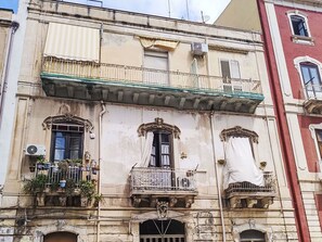 Un edificio con tres balcones, cada uno con barandilla pequeña y plantas en macetas.