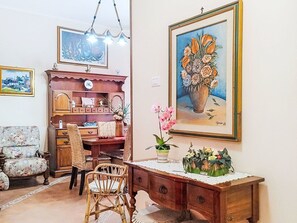 A room with a wooden desk, wicker chairs, a bookshelf, and a large framed painting of flowers.