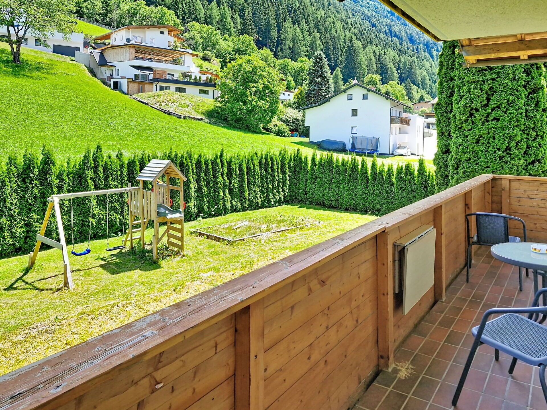 Eine Holzterrasse mit Schaukel und Blick auf eine grüne Landschaft mit Häusern.