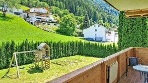 Eine Holzterrasse mit Schaukel und Blick auf eine grüne Landschaft mit Häusern.