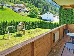 A wooden deck with a swing set and a view of a green landscape with houses. - Lovely apartment for 4 guests with WIFI, TV, terrace and pets allowed (Wenns)