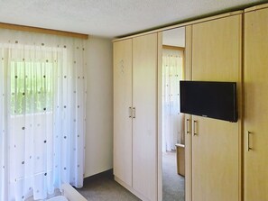 Ein Zimmer mit Kleiderschrank, Wandfernseher und einem mit Vorhängen versehenen Fenster.