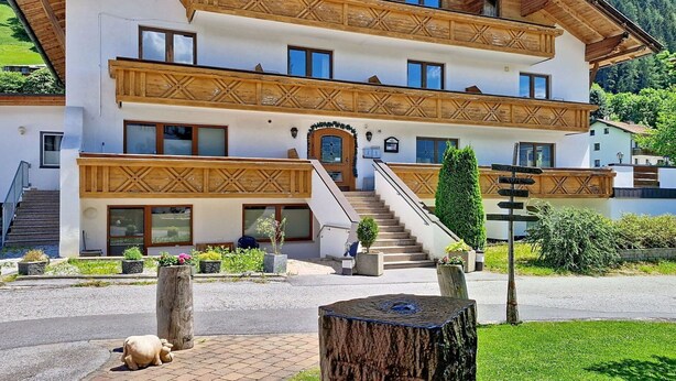 Ein mehrgeschossiges Gebäude mit einer traditionellen Holzfassade, einer Treppe, die zum Eingang führt, und einem Wegweiser mit Pfeilen.