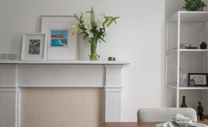 A dining area with a white fireplace, a vase of flowers, and a bookshelf. - Regents Park views - light filled studio, 1 min to Baker St tube. (London)