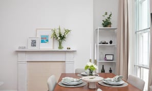 A dining area with a table set for four, a fireplace, and a bookshelf with decorative items. - Regents Park views - light filled studio, 1 min to Baker St tube. (London)