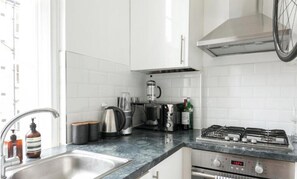 A modern kitchen with white cabinets, a stainless steel sink, a coffee maker, a kettle, and a gas stove. - Regents Park views - light filled studio, 1 min to Baker St tube. (London)