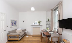 A modern living room with a sofa, a dining table, and a flat-screen TV. - Regents Park views - light filled studio, 1 min to Baker St tube. (London)