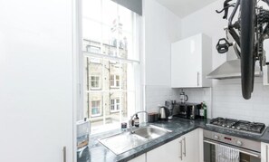 A modern kitchen with a large window, stainless steel appliances, and white cabinetry. - Regents Park views - light filled studio, 1 min to Baker St tube. (London)