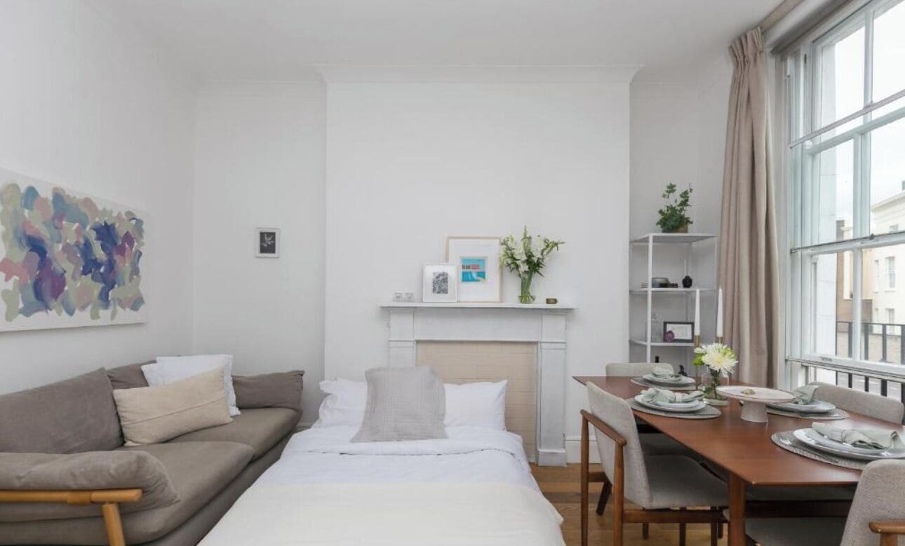 Une chambre d’hôtel moderne équipée d’un lit, d’un canapé, d’une table à manger pour deux personnes, d’une cheminée et d’une grande fenêtre avec des rideaux.