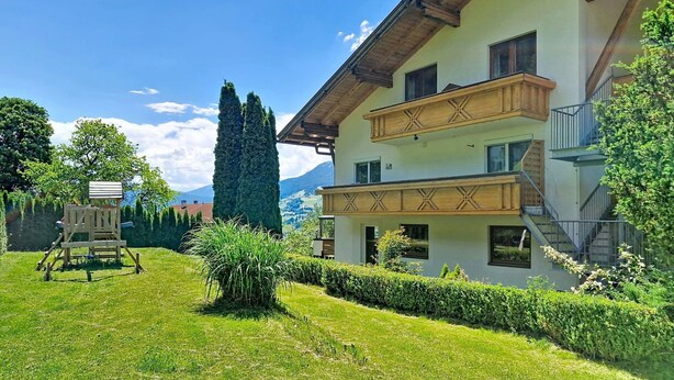 Ein zweistöckiges Gebäude mit einem Balkon, umgeben von einem gepflegten Rasen und Bäumen.