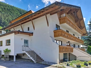 A multi-story building with a sloped roof, wooden balconies, and a staircase leading to the entrance. - Nice apartment for 3 guests with WIFI, TV, terrace and pets allowed (Wenns)
