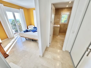Ein Schlafzimmer mit Bett, ein Badezimmer mit Waschbecken und Blick ins Freie.