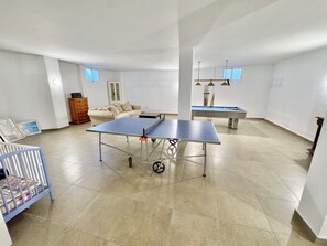 Ein geräumiges Zimmer mit Tischtennisplatte, Babybett und Schlafsofa.