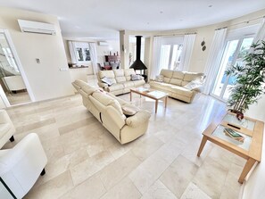 Ein großzügiges Wohnzimmer mit einem beigefarbenen Ecksofa, einem Glastisch und einem Essbereich im Hintergrund.