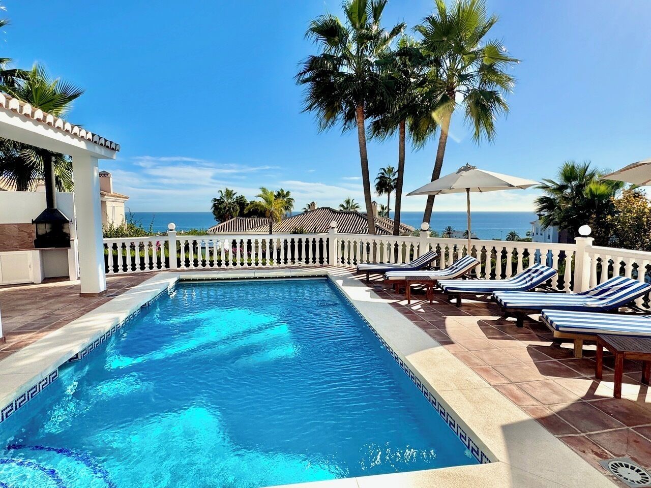 A swimming pool with lounge chairs and palm trees, overlooking a body of water.