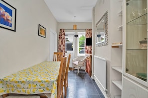 Ein Zimmer mit Esstisch, Stühlen, Heizkörper, Fernseher und Spiegel.