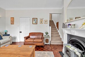 Een woonkamer met een bruine leren bank, een houten salontafel, een open haard en een trap die naar een hoger niveau leidt.