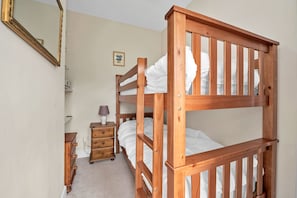 Een stapelbed met houten frame, een nachtkastje met lamp en een kleine dressoir.