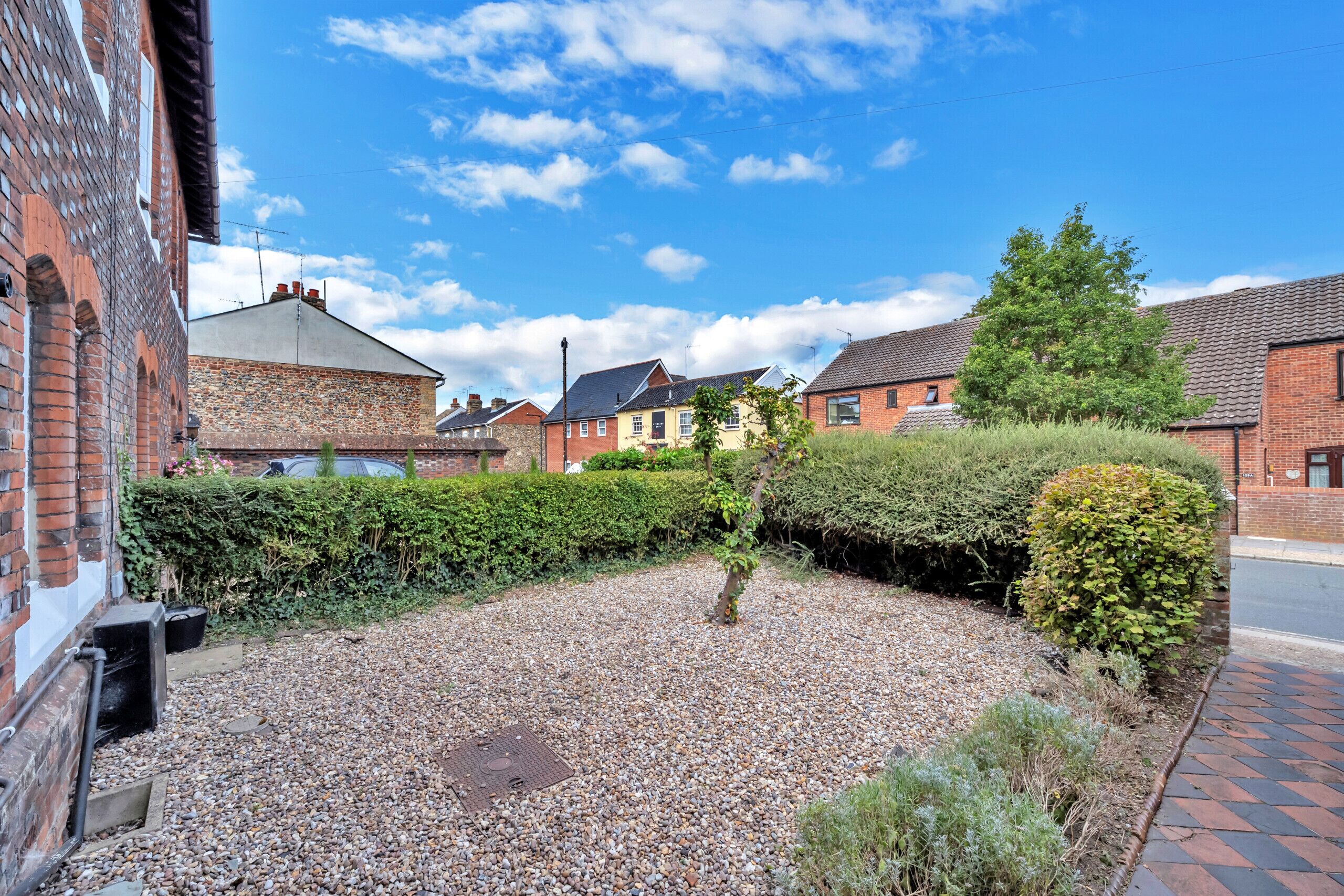 A residential area with a gravel driveway, a hedge, and houses with brick facades.