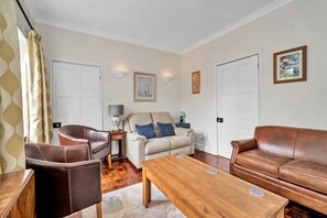 A living room with a brown leather sofa, a beige sofa with blue cushions, a wooden coffee table, and a brown leather armchair. - The Jewel In Bury (Bury St Edmunds)