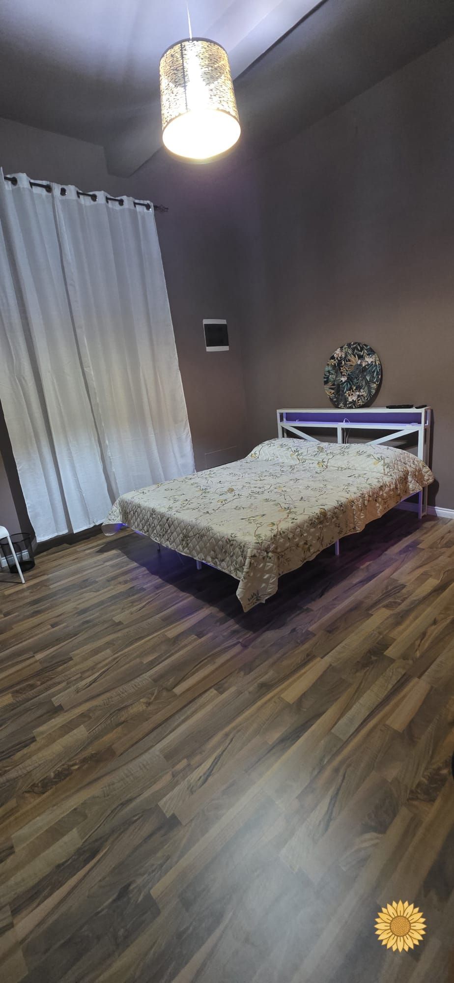 Ein Schlafzimmer mit einem Bett, einer Deckenleuchte, einem Vorhang und einer Wanddekoration.