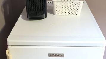 A white refrigerator with a logo on the front, a black appliance on top, and a white basket beside it.