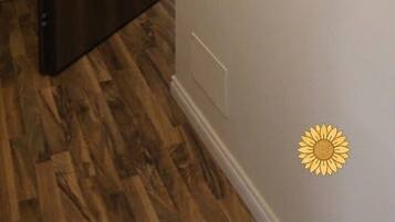 A hallway with a wooden door, a wall-mounted mirror, a small shelf with decorative items, and a hanging light fixture.