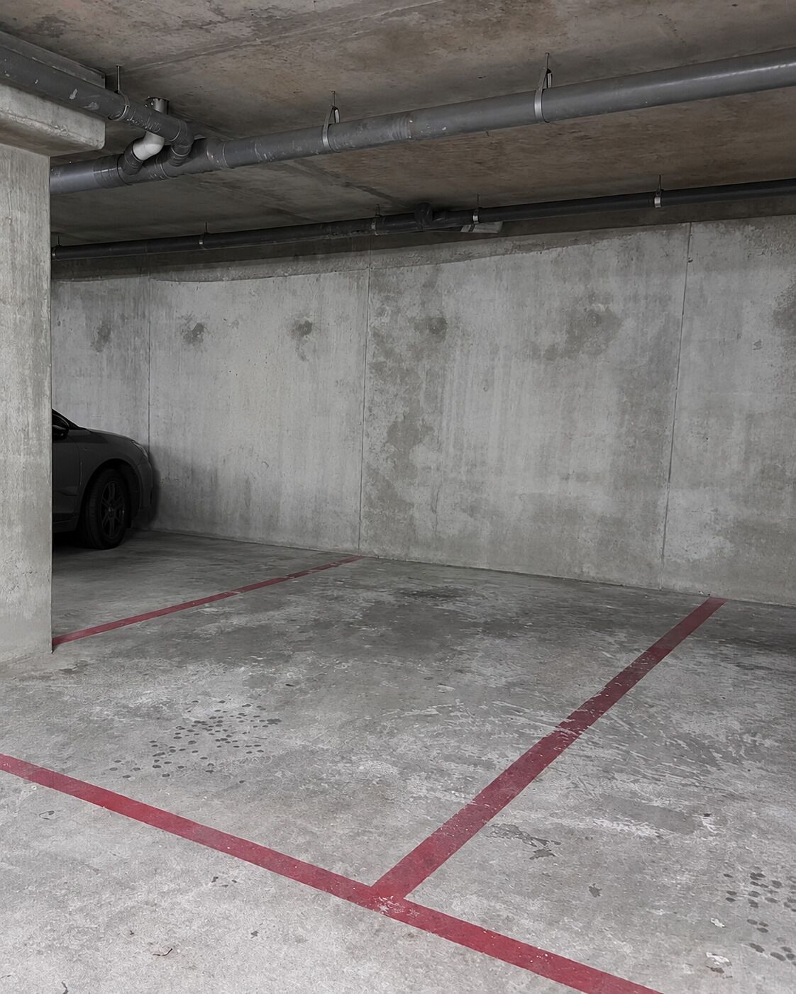 Un estacionamiento con paredes de concreto y un auto estacionado al fondo.