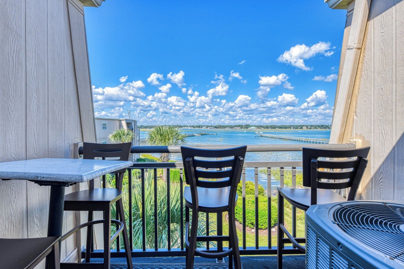 A balcony with a table and chairs, overlooking a body of water and a pier.