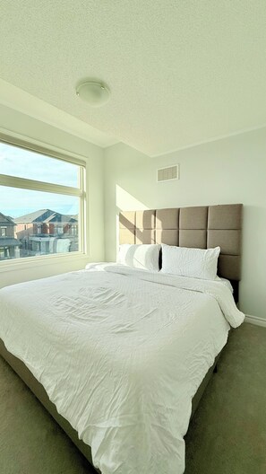 A bedroom with a large bed, a window, and a view of buildings outside. - Sleeps 14 | The Snow Valley Escape, Barrie | Entire House (Springwater)