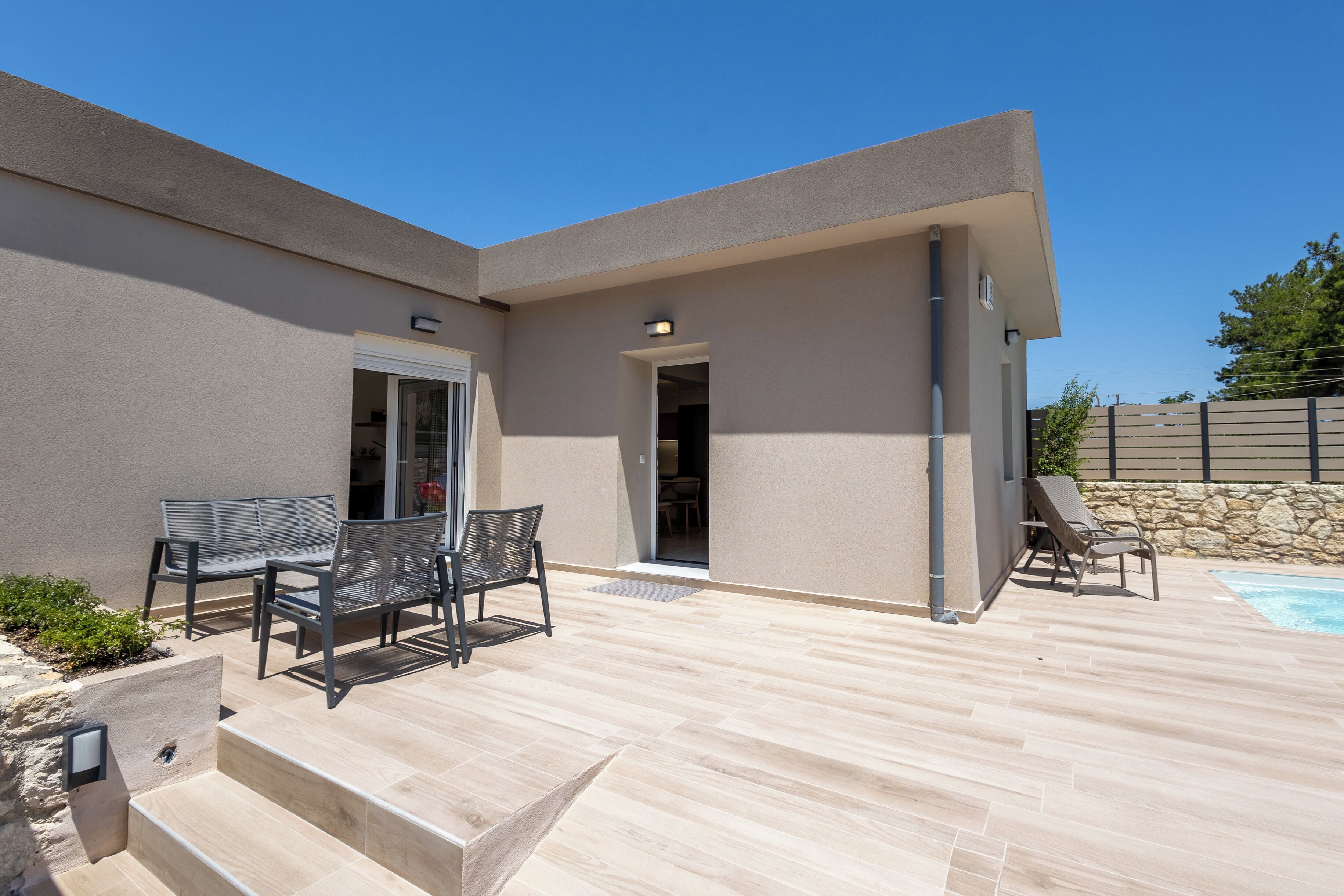 Un patio moderno al aire libre con piscina, una zona de estar cubierta y un muro de piedra.