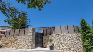 A stone wall entrance with a metal gate, a potted plant, and a clear blue sky. - Eltynia Luxury Villa (KOUNAVOI)