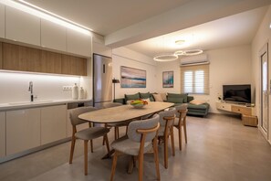 Eine moderne Küche mit eingebauten Geräten, ein Essbereich mit Holztisch und -stühlen sowie ein Wohnbereich mit einer Couch und einem Flachbildfernseher.