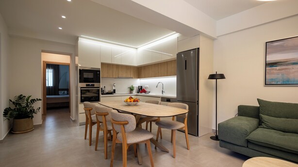 A modern kitchen with a central island, wooden chairs, a dining table, and a refrigerator. - Eltynia Luxury Villa (KOUNAVOI)