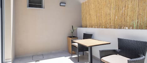A patio area with a table and two chairs, a small window, and a bamboo fence.